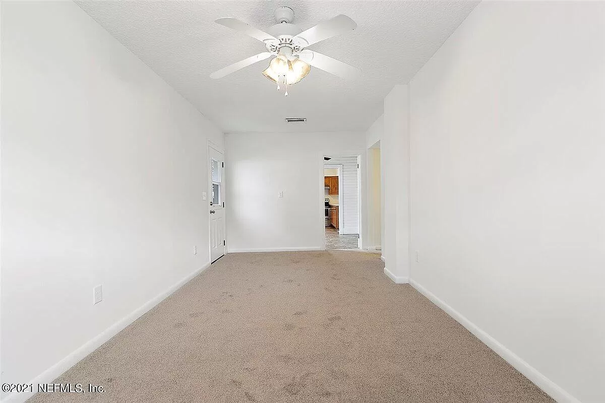 A large empty living room that leads into a kitchen