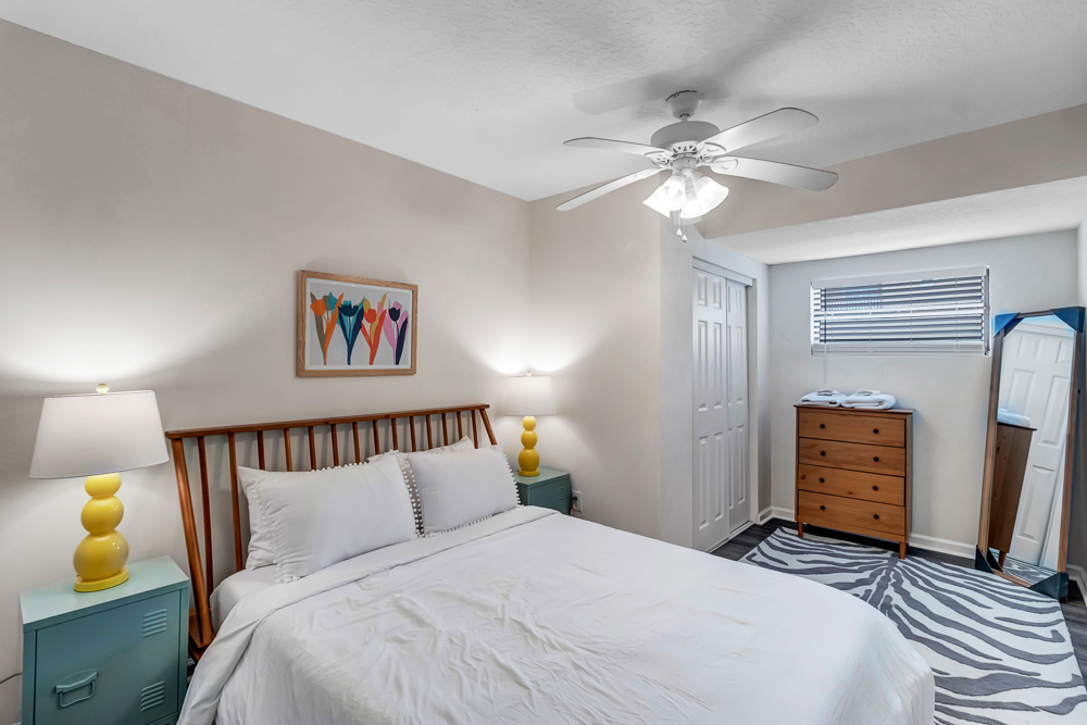 A boutique hotel bedroom is decorated with furniture, bedding, linens, window treatments, lamps, and a ceiling fan, creating a cozy and inviting atmosphere.