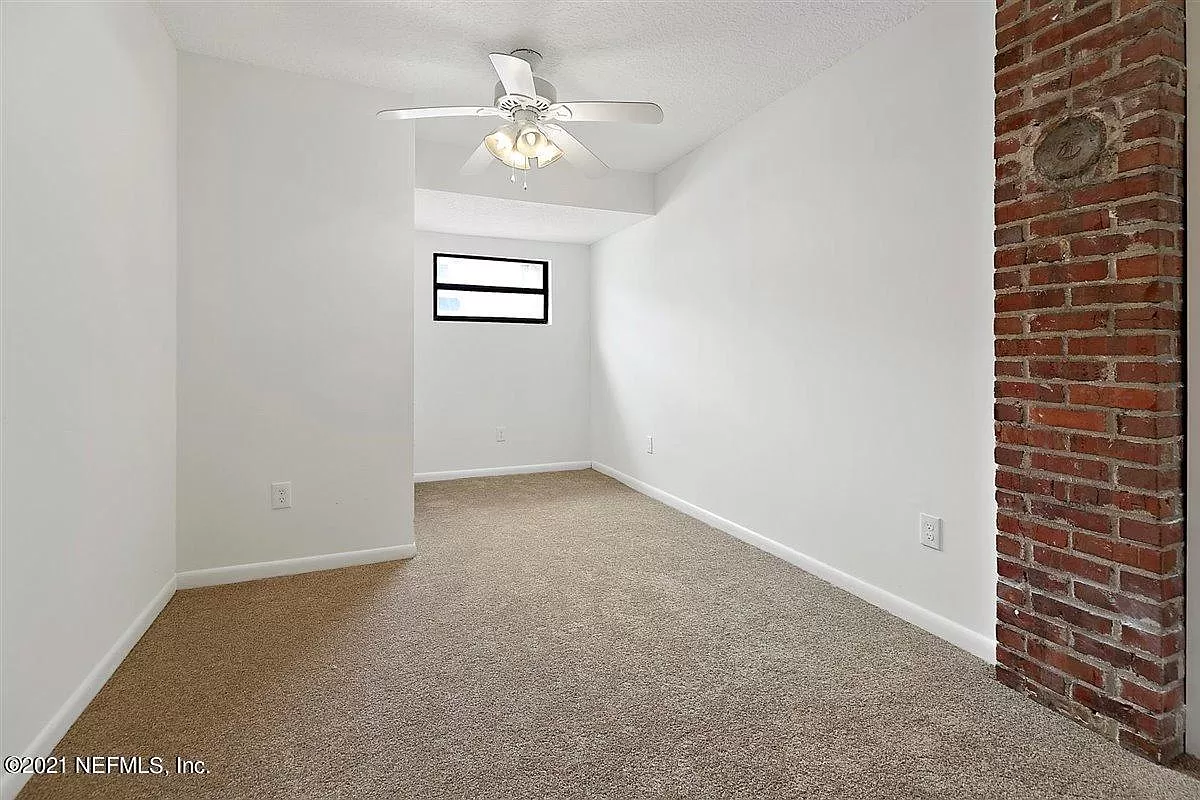 An empty room with a ceiling fan and window and some an exposed brick wall
